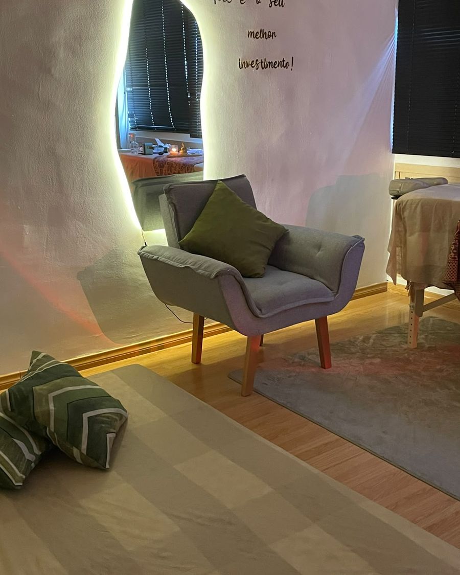 Poltrona com almofada verde ao lado de espelho iluminado na segunda sala